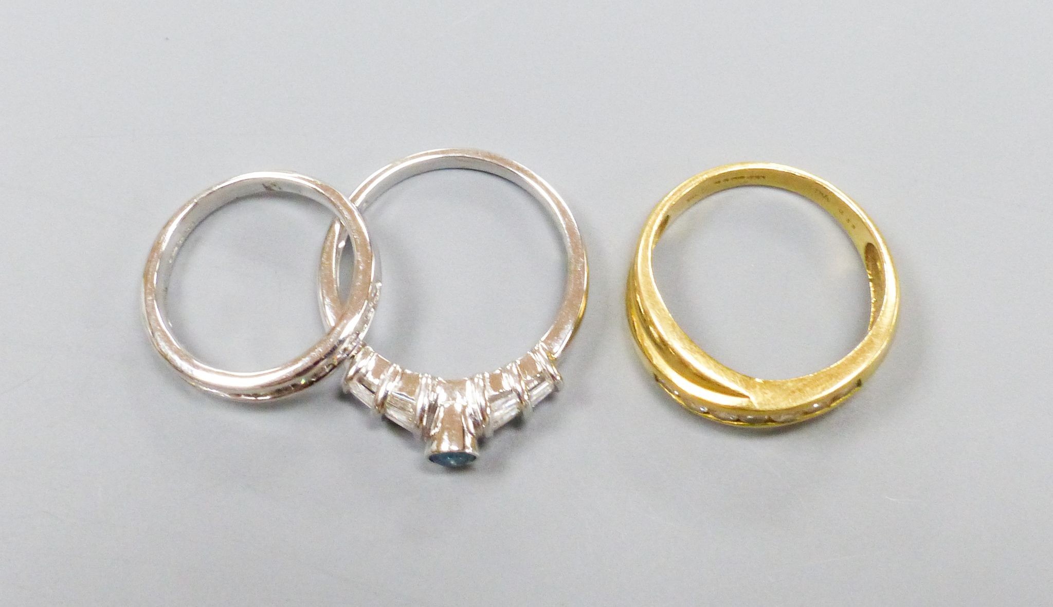 Three modern dress rings including a 750 yellow metal and seven stone channel set diamond crossover ring, size O, an 18ct white gold and nine stone diamond set half eternity ring, size I and a 750 white metal and blue di